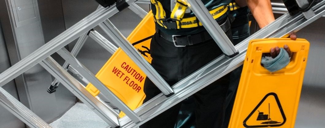 Construction worker with ladder and wet floor signage